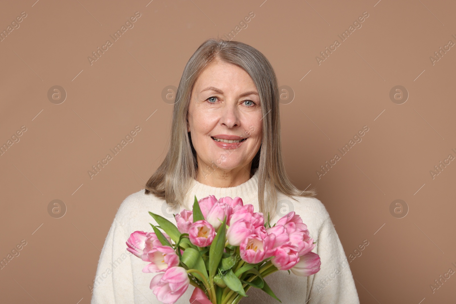 Photo of Smiling woman with bouquet of tulips on beige background