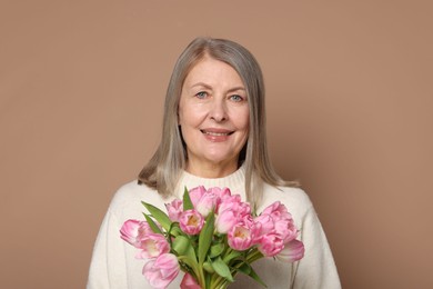 Smiling woman with bouquet of tulips on beige background