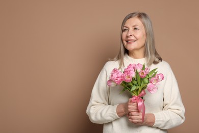 Photo of Smiling woman with bouquet of tulips on beige background. Space for text