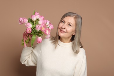 Smiling woman with bouquet of tulips on beige background