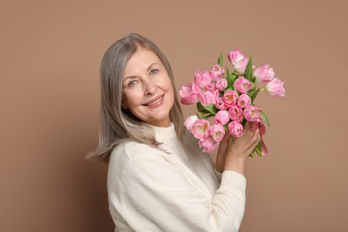 Smiling woman with bouquet of tulips on beige background