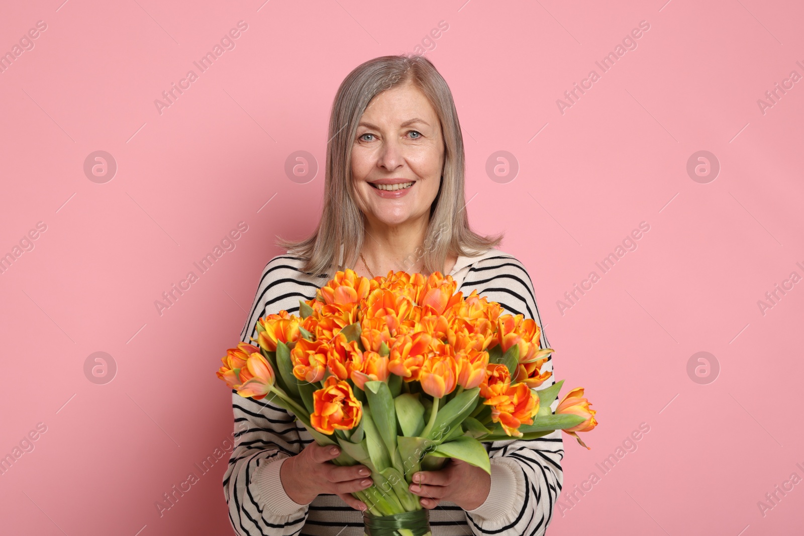 Photo of Smiling woman with bouquet of tulips on pink background