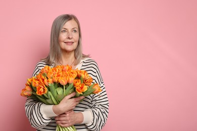 Smiling woman with bouquet of tulips on pink background. Space for text