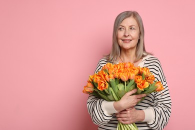 Smiling woman with bouquet of tulips on pink background. Space for text