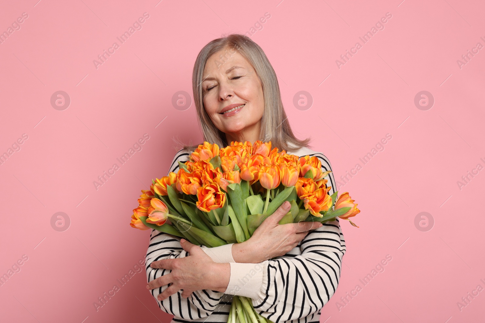 Photo of Smiling woman with bouquet of tulips on pink background