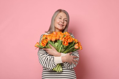 Smiling woman with bouquet of tulips on pink background