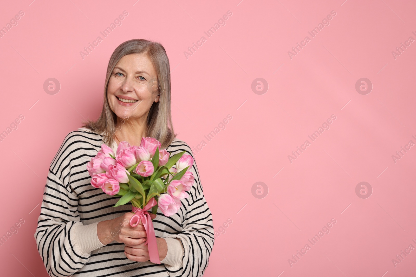 Photo of Smiling woman with bouquet of tulips on pink background. Space for text