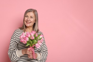 Smiling woman with bouquet of tulips on pink background. Space for text