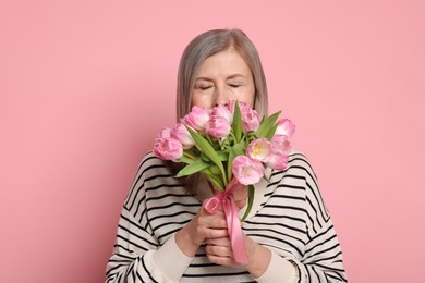 Beautiful woman with bouquet of tulips on pink background