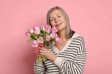 Beautiful woman with bouquet of tulips on pink background