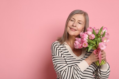 Smiling woman with bouquet of tulips on pink background. Space for text