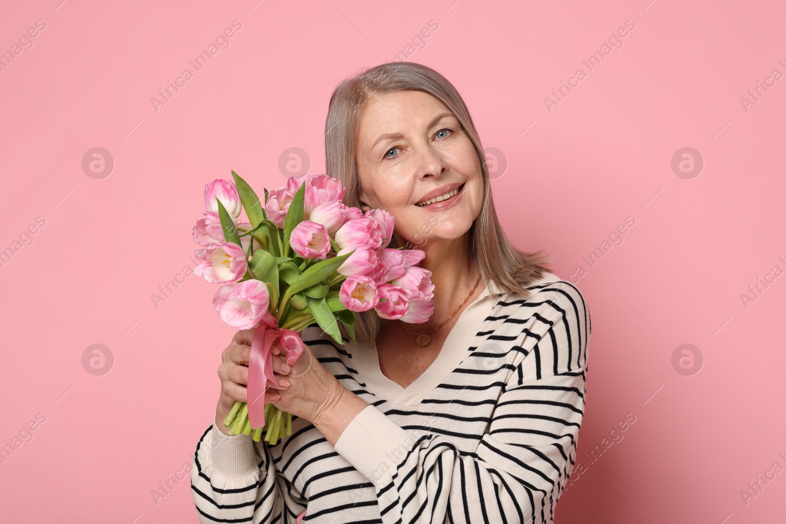 Photo of Smiling woman with bouquet of tulips on pink background