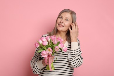 Photo of Smiling woman with bouquet of tulips on pink background