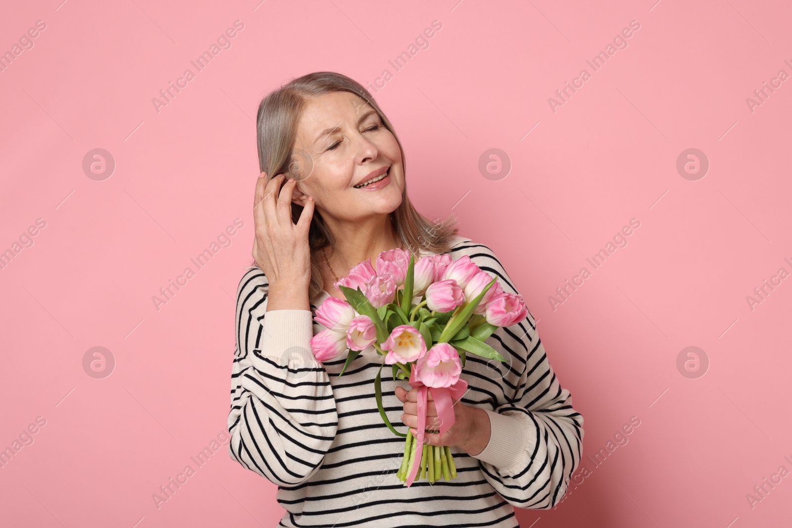 Photo of Smiling woman with bouquet of tulips on pink background