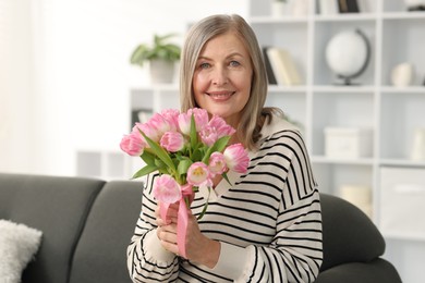 Photo of Smiling woman with bouquet of tulips on sofa at home