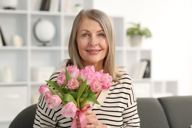 Smiling woman with bouquet of tulips on sofa at home