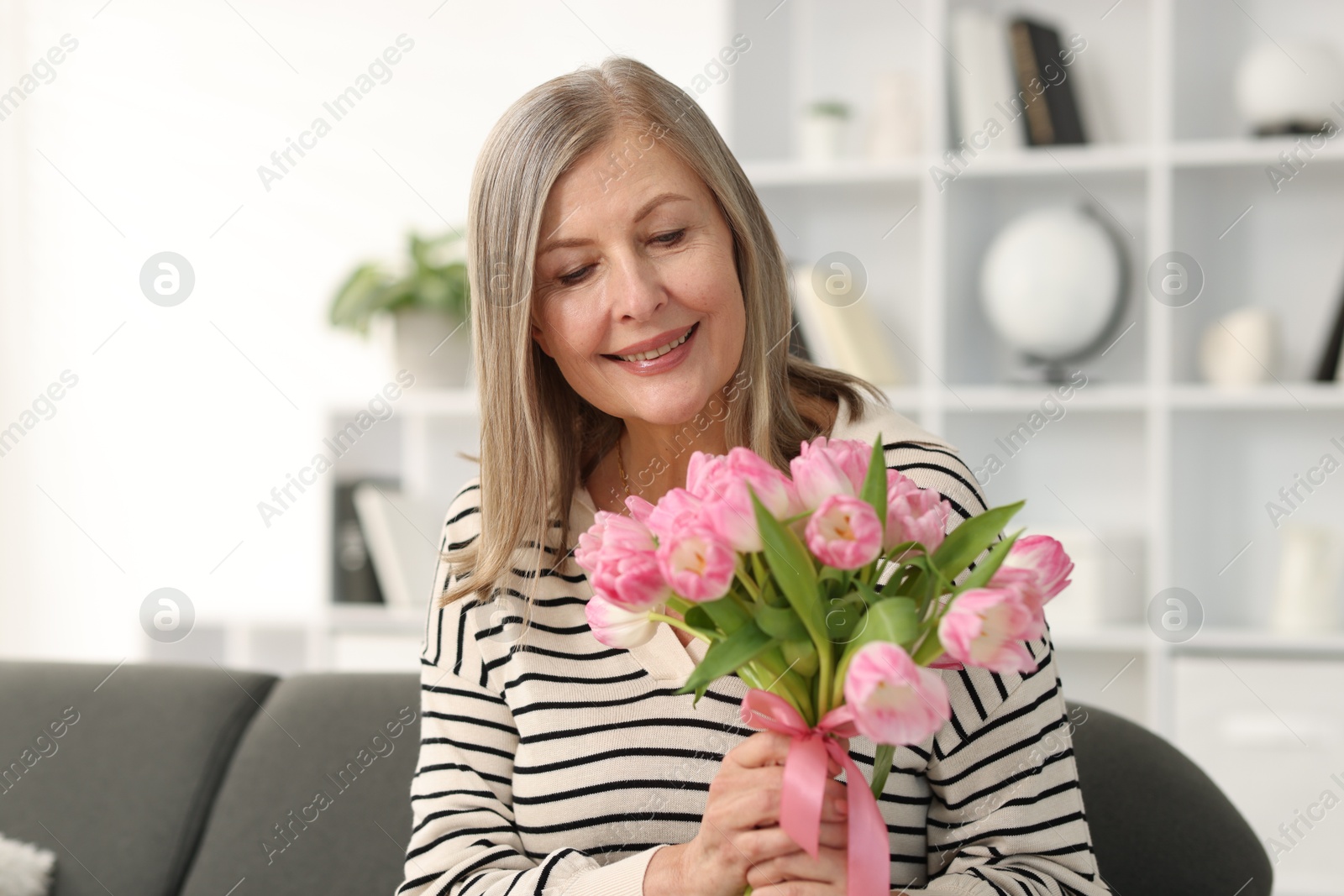 Photo of Smiling woman with bouquet of tulips on sofa at home