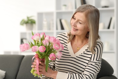 Smiling woman with bouquet of tulips on sofa at home