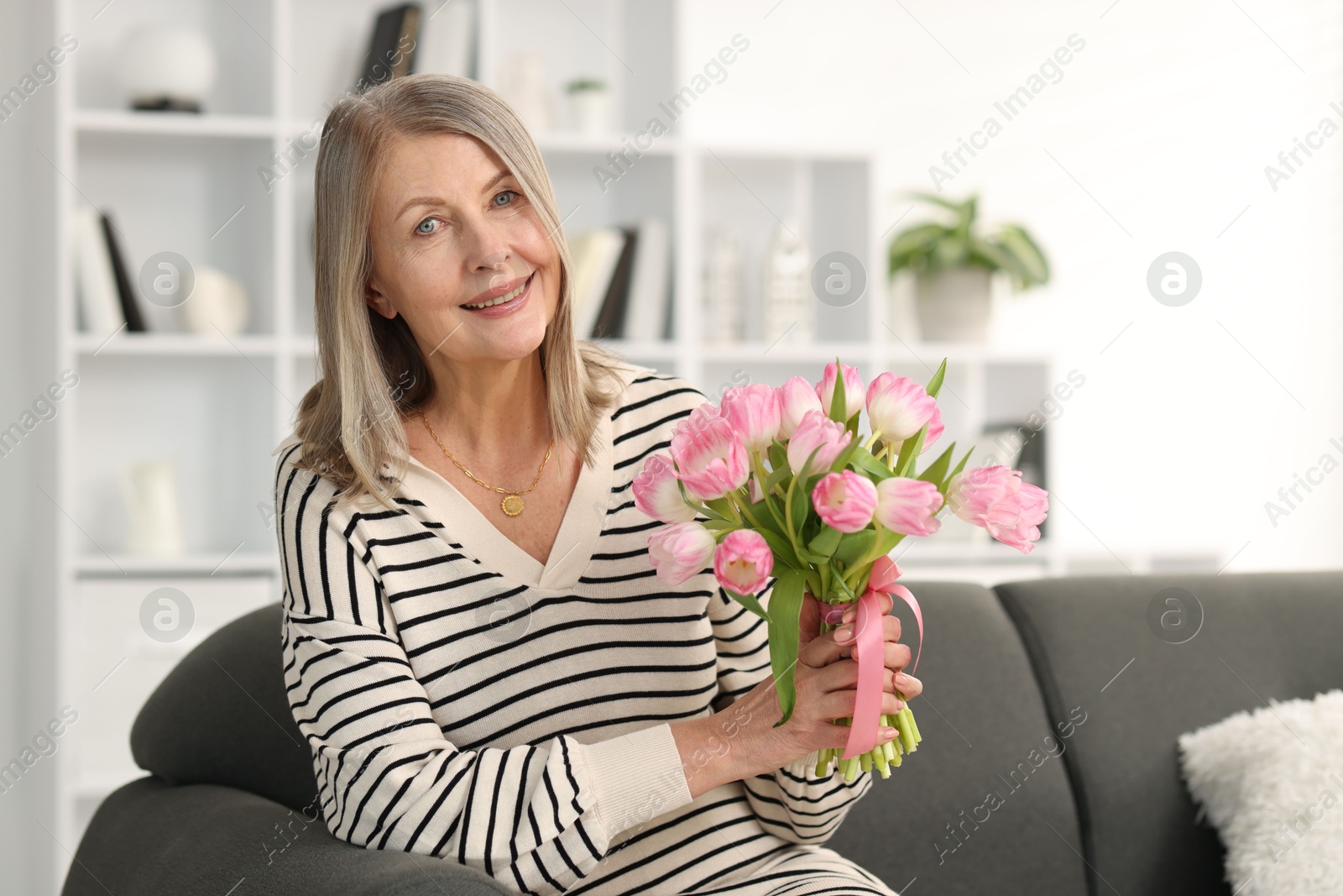 Photo of Smiling woman with bouquet of tulips on sofa at home