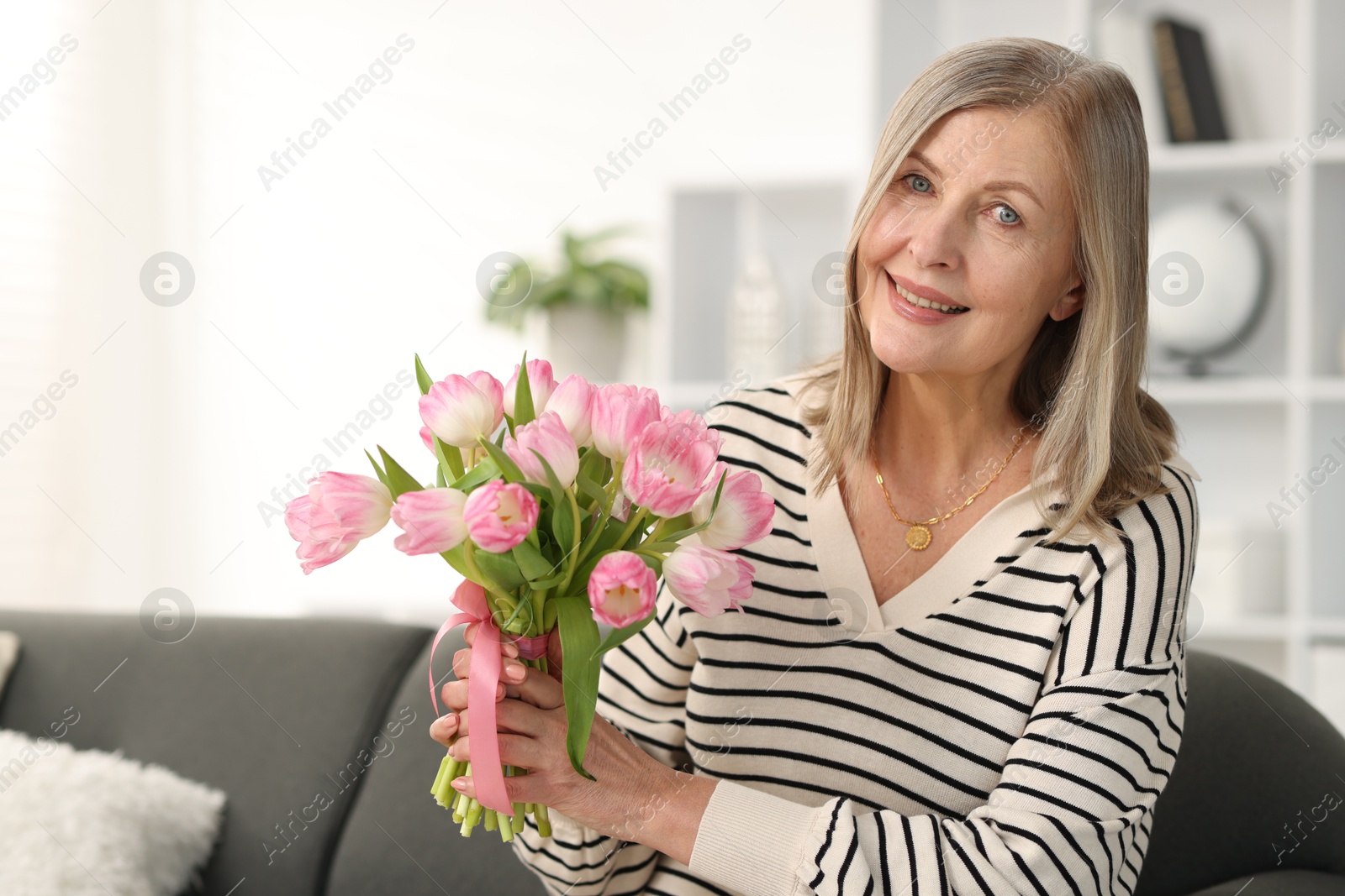 Photo of Smiling woman with bouquet of tulips on sofa at home