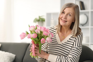 Smiling woman with bouquet of tulips on sofa at home