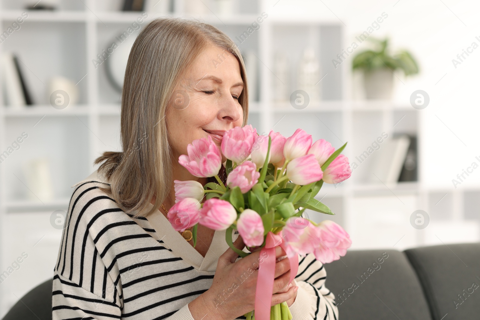 Photo of Beautiful woman with bouquet of tulips at home