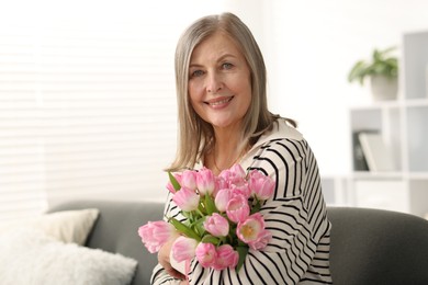 Photo of Smiling woman with bouquet of tulips on sofa at home