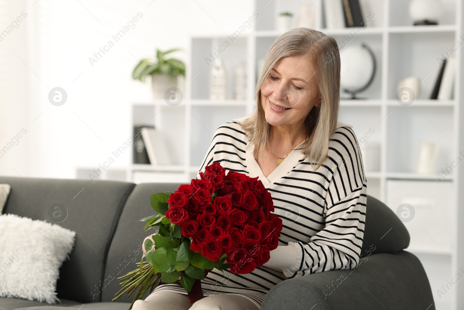 Photo of Smiling woman with bouquet of roses on sofa at home