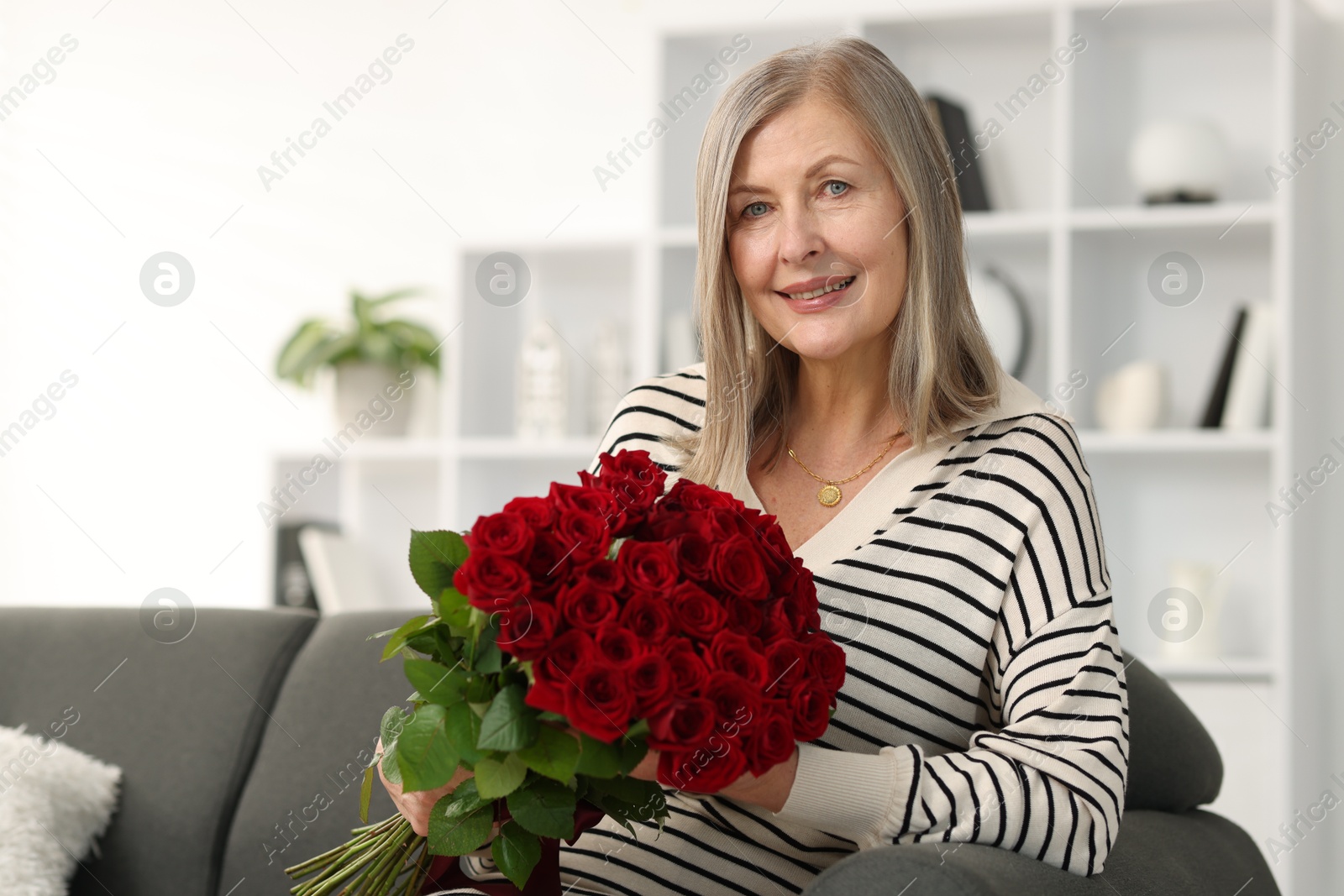 Photo of Smiling woman with bouquet of roses on sofa at home