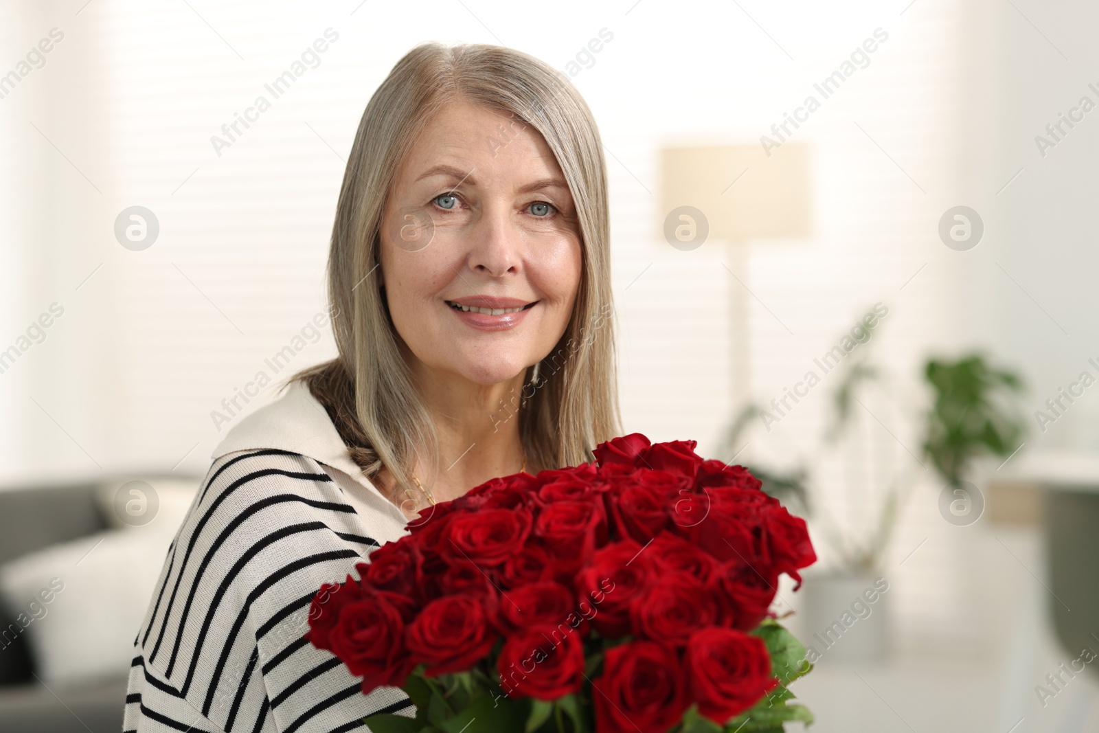 Photo of Smiling woman with bouquet of roses at home