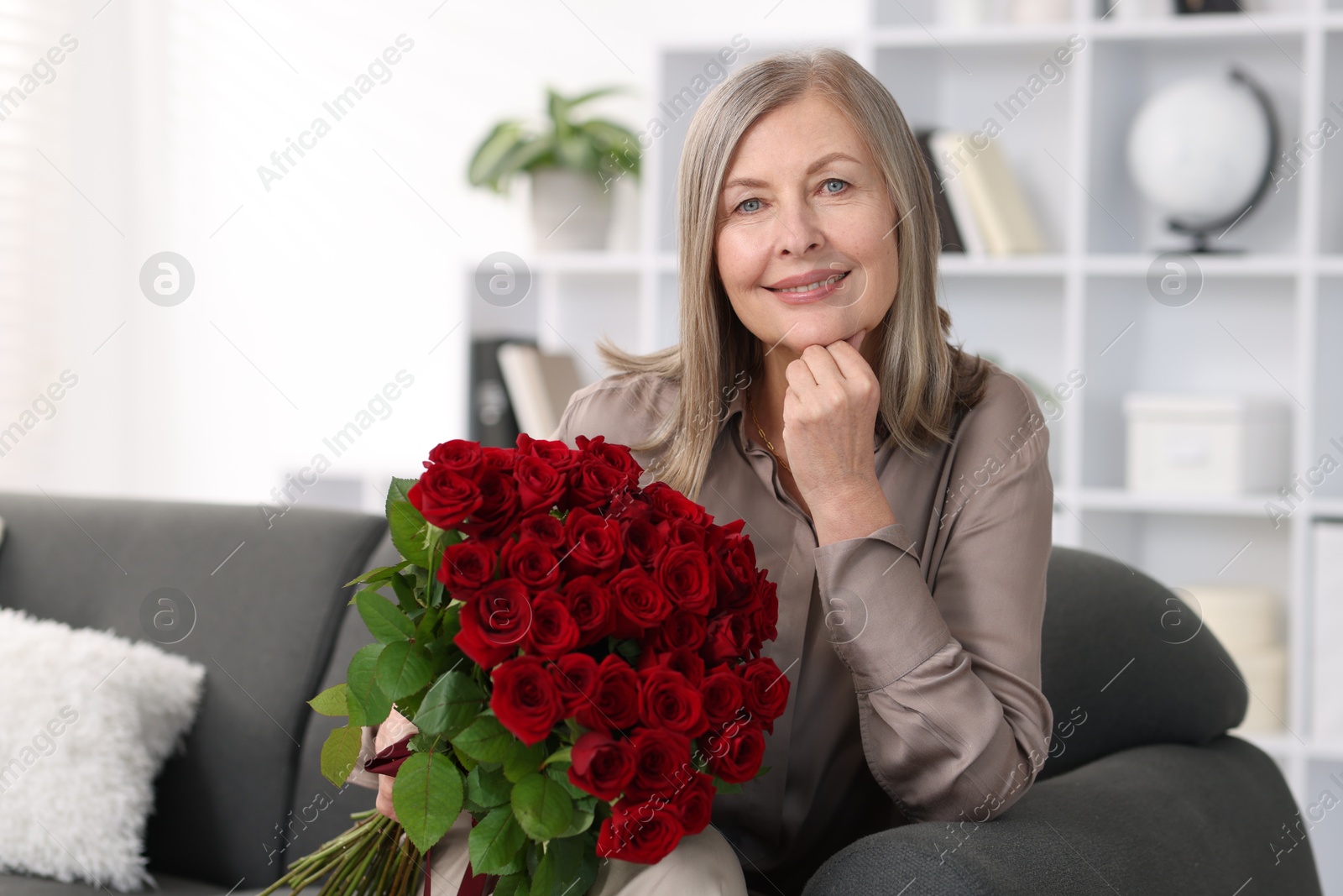 Photo of Smiling woman with bouquet of roses on sofa at home