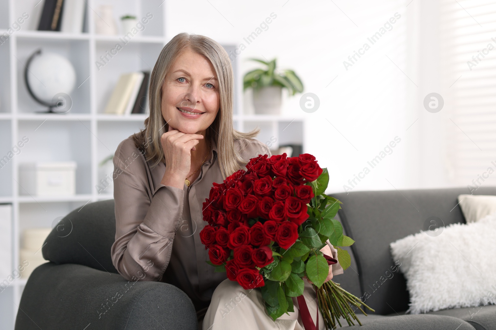 Photo of Smiling woman with bouquet of roses on sofa at home