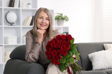 Smiling woman with bouquet of roses on sofa at home