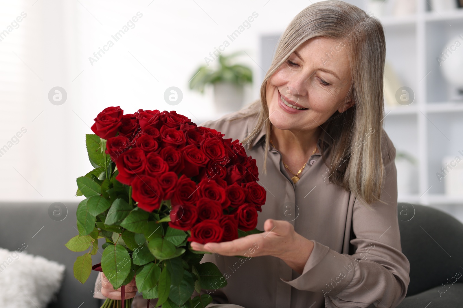 Photo of Smiling woman with bouquet of roses on sofa at home