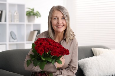 Photo of Smiling woman with bouquet of roses on sofa at home