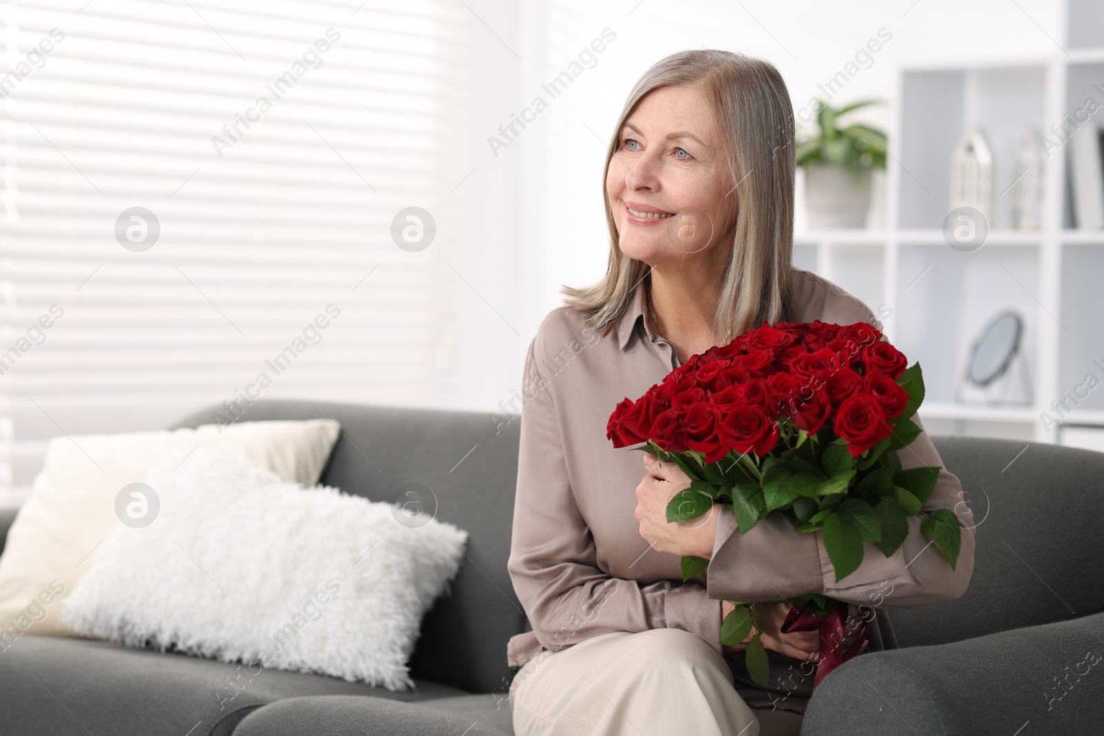 Photo of Smiling woman with bouquet of roses on sofa at home