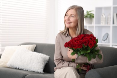 Smiling woman with bouquet of roses on sofa at home