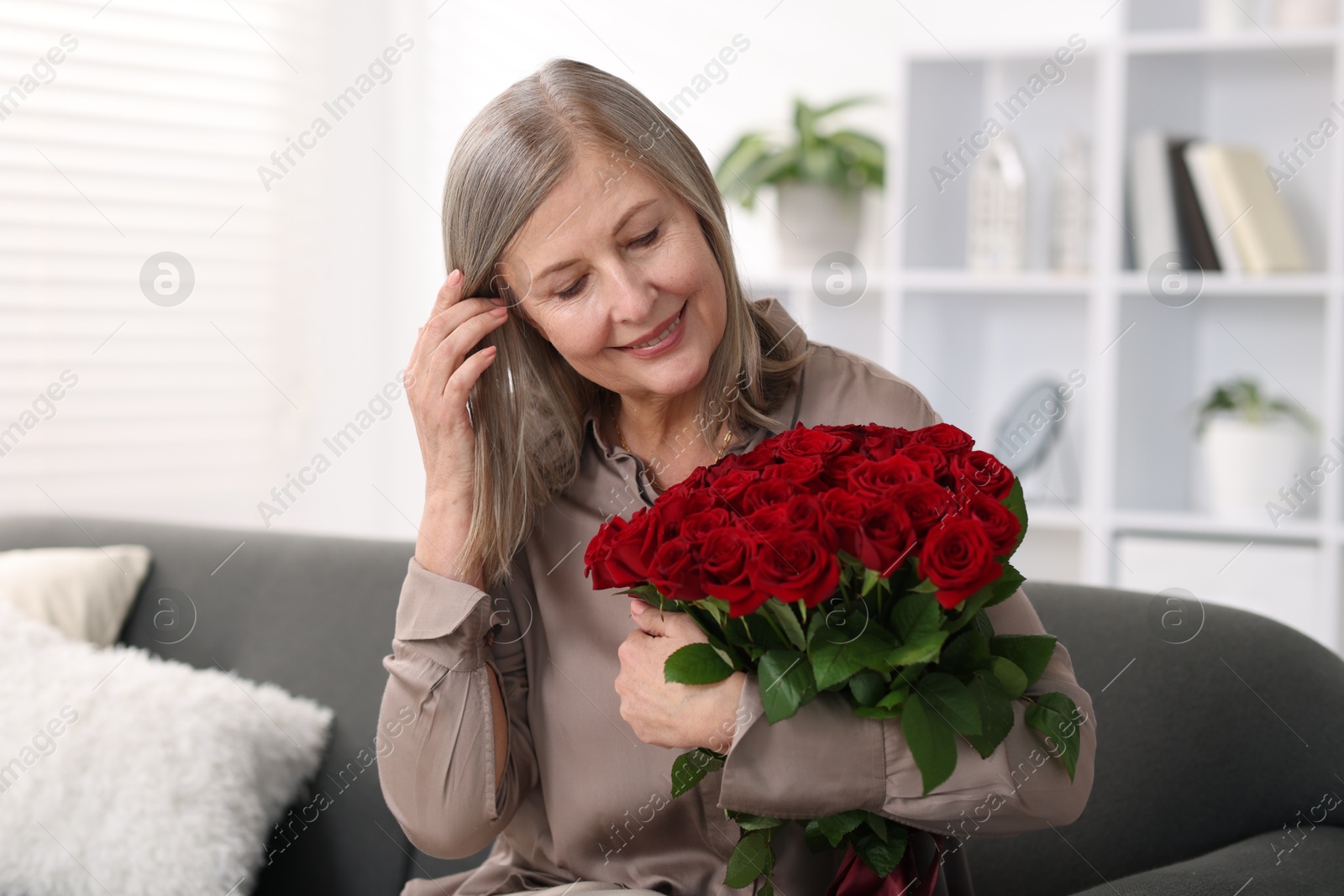 Photo of Smiling woman with bouquet of roses on sofa at home