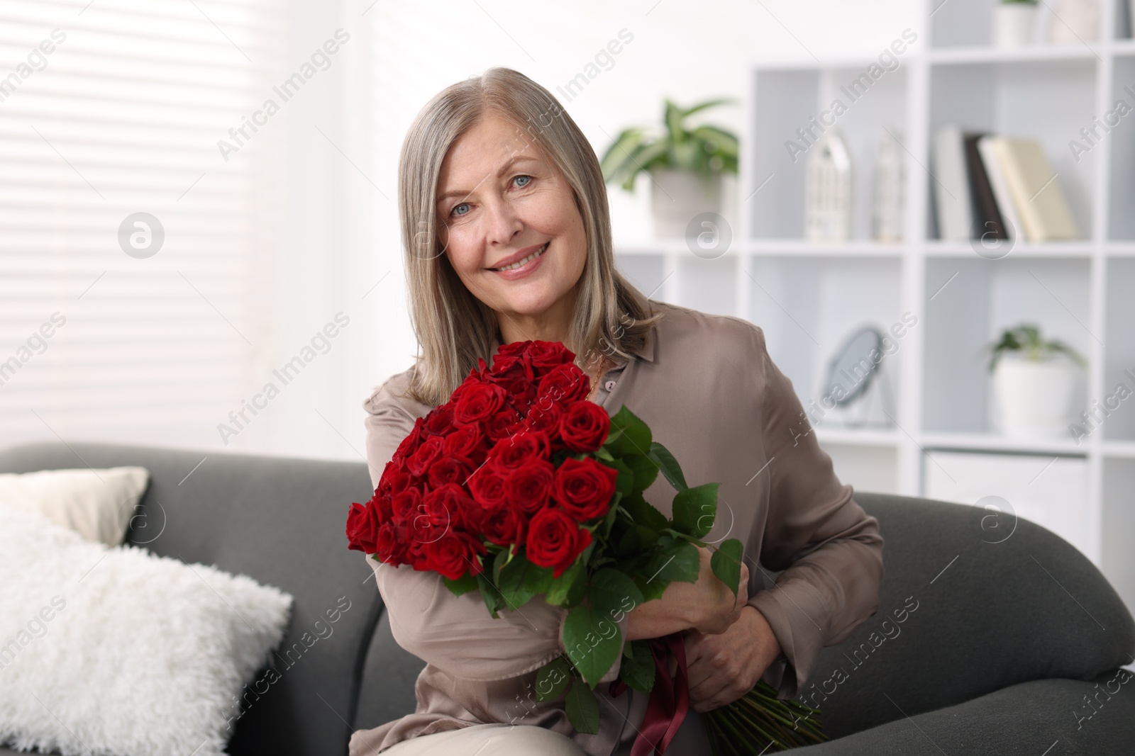 Photo of Smiling woman with bouquet of roses on sofa at home