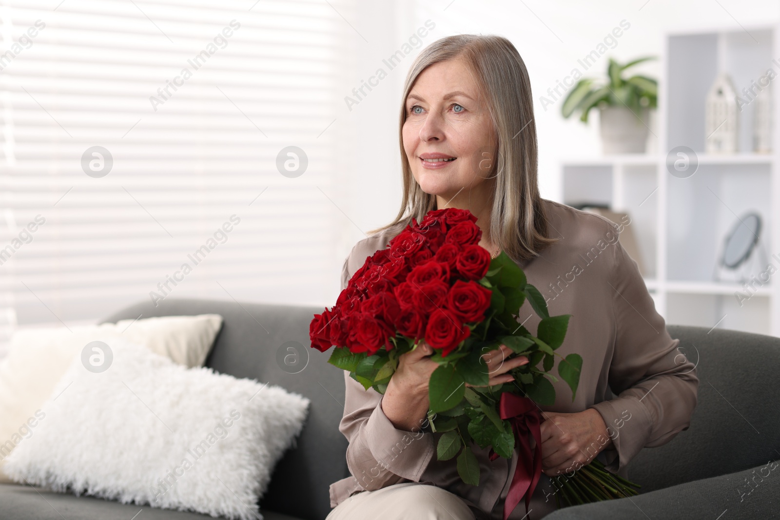 Photo of Smiling woman with bouquet of roses on sofa at home