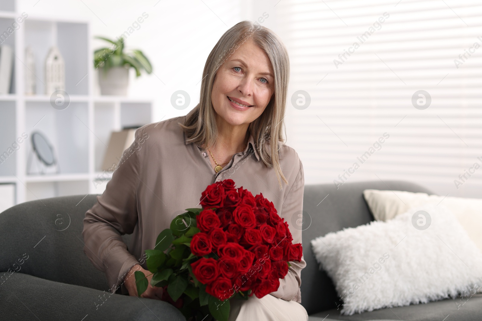 Photo of Smiling woman with bouquet of roses on sofa at home