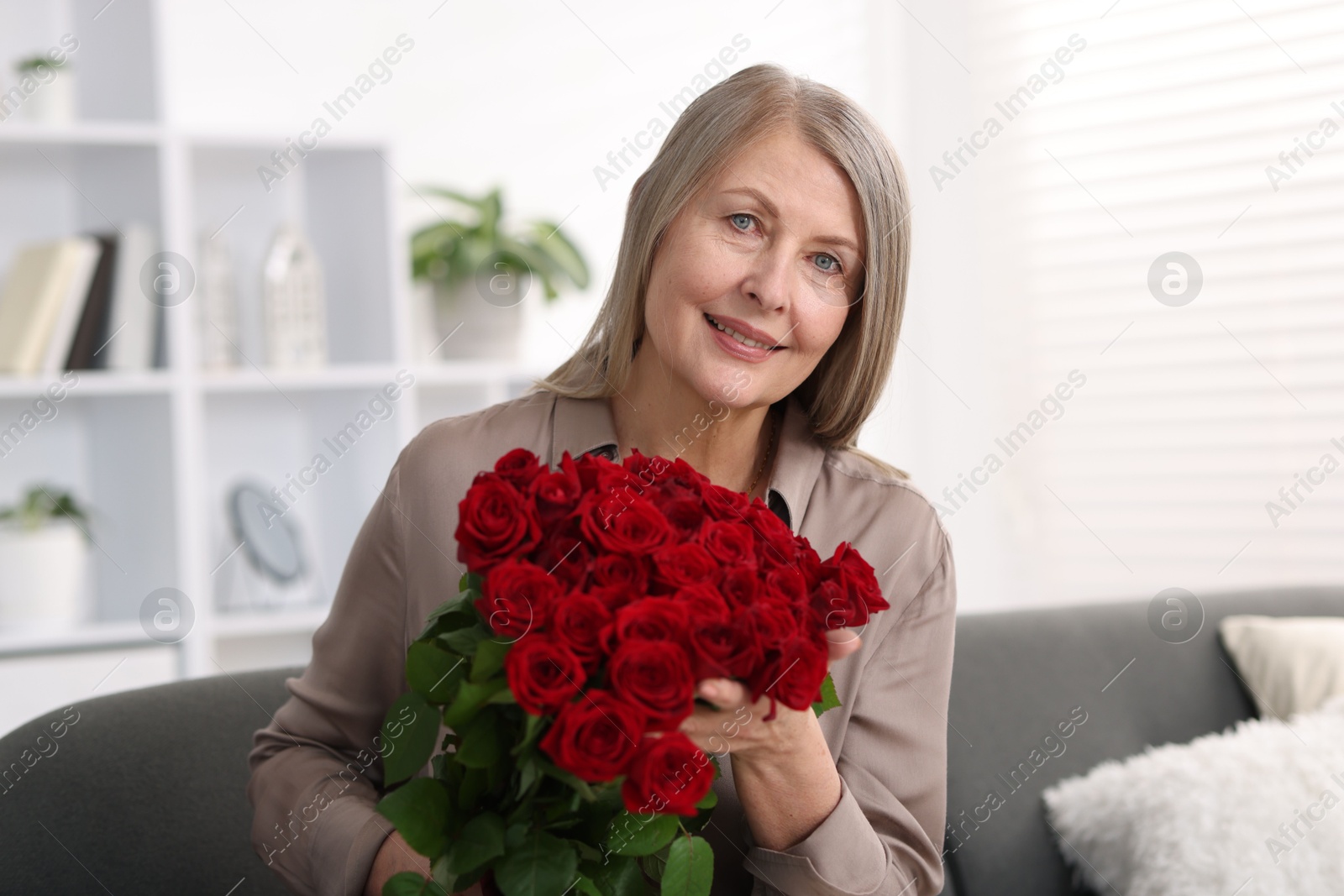 Photo of Smiling woman with bouquet of roses on sofa at home