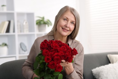 Smiling woman with bouquet of roses on sofa at home