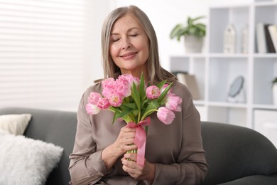 Smiling woman with bouquet of tulips on sofa at home