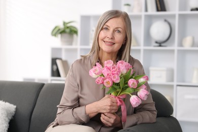 Smiling woman with bouquet of tulips on sofa at home