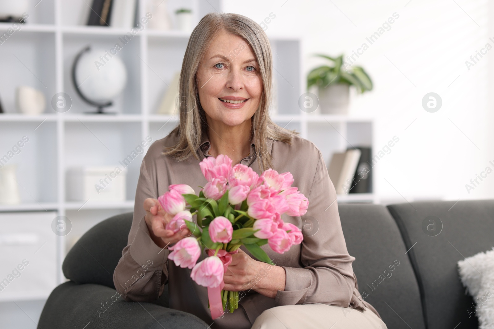 Photo of Smiling woman with bouquet of tulips on sofa at home