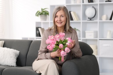 Photo of Smiling woman with bouquet of tulips on sofa at home