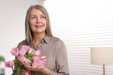 Photo of Smiling woman with bouquet of tulips at home. Space for text