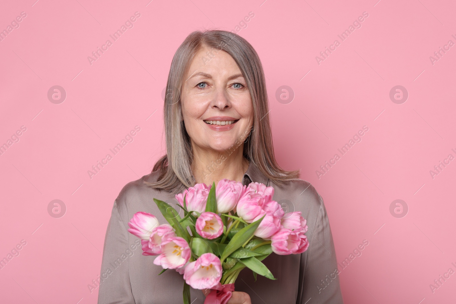 Photo of Smiling woman with bouquet of tulips on pink background