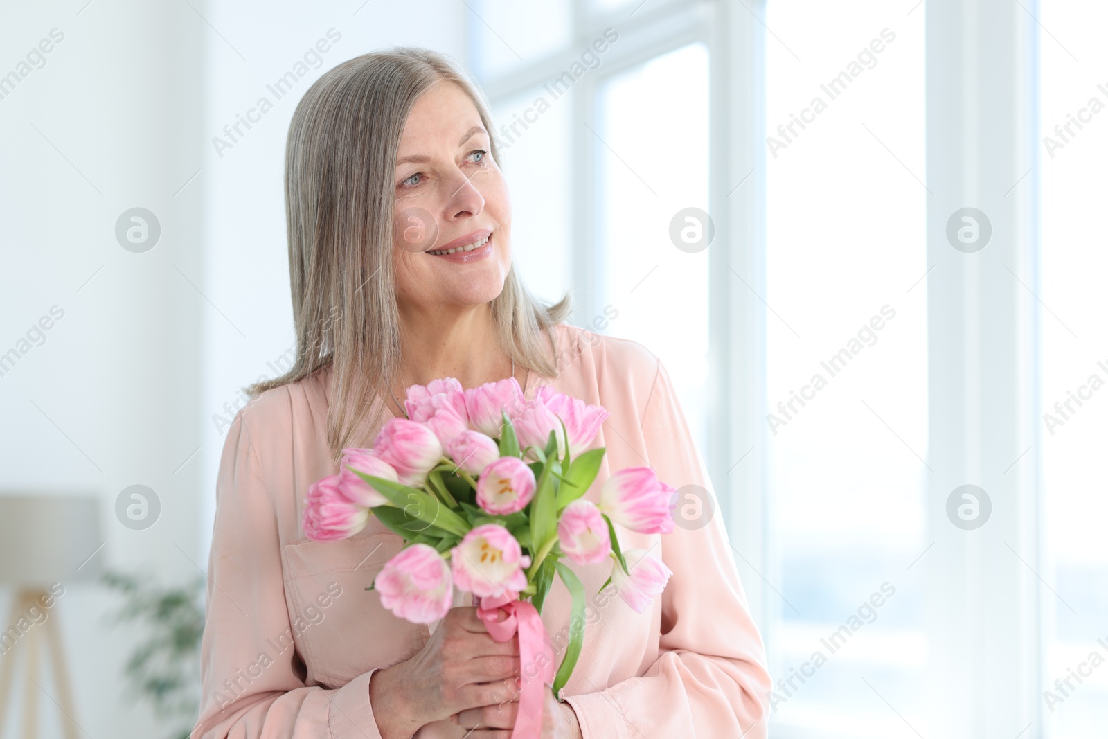 Photo of Smiling woman with bouquet of tulips at home. Space for text